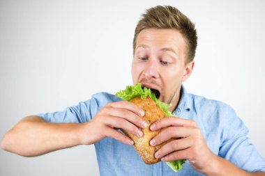 genç yakışıklı aç adam izole beyaz arka plan üzerinde salata yaprağı ile taze sandviç yiyor