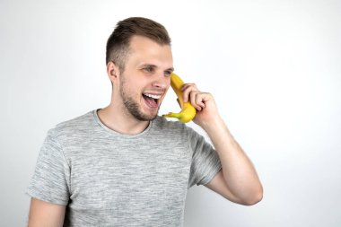 izole beyaz arka plan üzerinde konuşma sırasında gülümseyerek kulağının yanında bir akıllı telefon gibi taze muz tutan genç yakışıklı adam