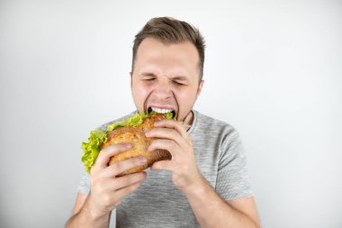izole beyaz arka plan üzerinde salata yaprağı ile taze sandviç ısırma kapalı gözleri ile genç yakışıklı aç adam