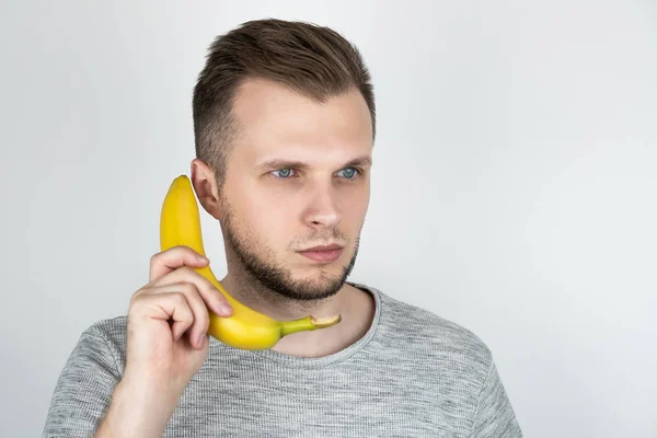 Jovem bonito homem segurando banana fresca como um smartphone perto de sua orelha no isolado fundo branco — Fotografia de Stock