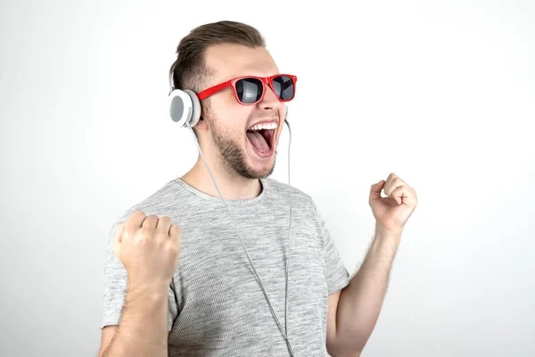 Joven hombre guapo con gafas de sol rojas bailando felizmente en auriculares escuchando sus éxitos musicales favoritos sobre un fondo blanco aislado —  Fotos de Stock
