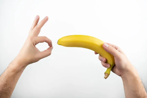 Imagem de mãos segurando banana fresca lidar com gestos sexuais no fundo branco isolado — Fotografia de Stock