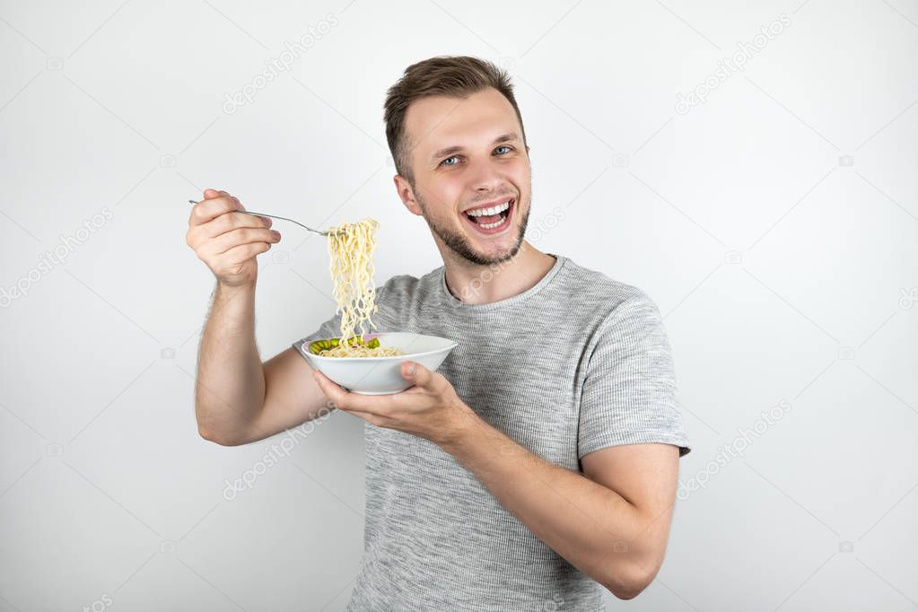 young handsome man eating noodles with fork looking hungry on isolated white background