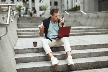genç yakışıklı ofis çalışanı dışında merdivenlerde otururken mola sırasında onun sandviç yerken ve öğle yemeği için kahve içerken tatsız iş sohbeti yapıyor