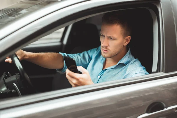 Jovem bonito homem dirige inseguro verificando seu smartphone em fuga — Fotografia de Stock