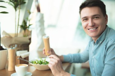 genç yakışıklı adam ofis yakınındaki kafede mola sırasında öğle yemeği için salata yiyor ve kahve içiyor mutlu görünüyor