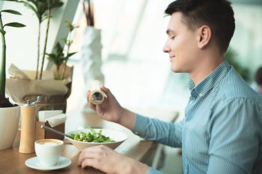 genç yakışıklı gülümseyen adam tuzlama salatası onun öğle yemeği yemek ve ofis yakınındaki kafede mola sırasında kahve içmeye hazırlanıyor