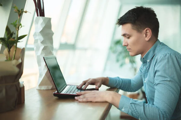 Joven hombre de negocios guapo trabaja en su computadora portátil mientras almuerza en la cafetería cerca de la oficina — Foto de Stock