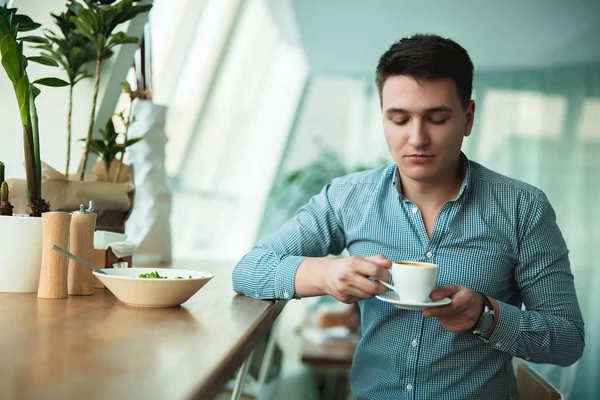 genç yakışıklı adam onun sıcak kahve içme ve ofis yakınındaki kafede mola sırasında öğle yemeği için salata yeme