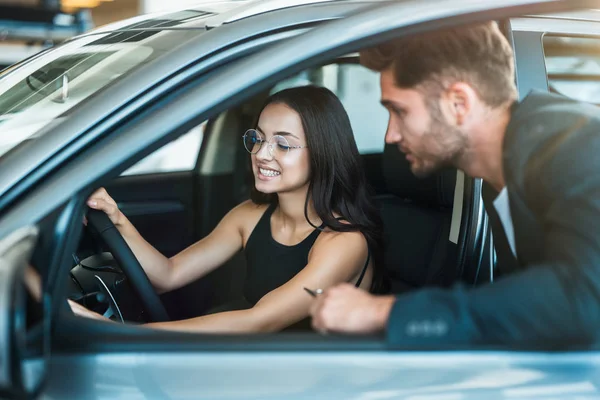 Hombre guapo gerente consultando joven hermosa mujer cliente al elegir un coche nuevo en concesionario — Foto de Stock