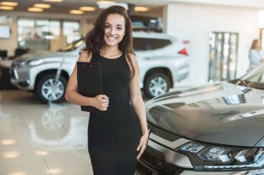 güzel esmer kadın yöneticisi bayilik merkezinde gülümseyerek ayakta broşür tutan