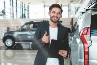 genç yakışıklı adam yöneticisi elinde elinde marka gibi gösteren yepyeni Suv yakın bayilik merkezinde ayakta broşür tutarak gülümseyen