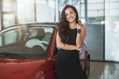 genç güzel kadın yepyeni bir araba satın alma bayilik merkezinde ayakta elinde araba anahtarları ile mutlu görünüyor