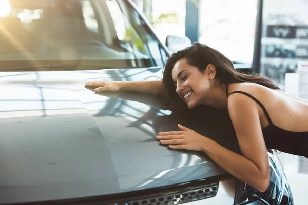 Bella bruna donna sentirsi felice abbracciando la sua auto nuova di zecca nel centro di distribuzione — Foto Stock