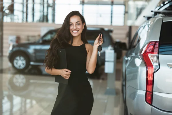 Bella bruna donna manager sorridente tenuta brochure in una mano e chiavi dell'auto in un altro in piedi nel centro di distribuzione vicino al nuovissimo SUV — Foto Stock