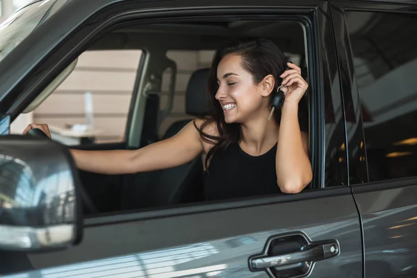 Bella donna bruna seduta in auto nuova di zecca dopo l'affare di successo nel centro di concessionaria alla ricerca di chiavi felici in possesso di auto — Foto Stock