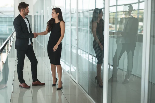 Dois parceiros de negócios jovem mulher bonita em vestido preto sexy e homem bonito apertando as mãos no escritório após negócio bem sucedido — Fotografia de Stock
