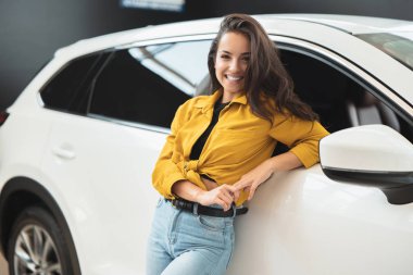güzel esmer kadın mutlu görünümlü beyaz araç yaslanmış bayilik merkezinde yeni bir araba arıyor