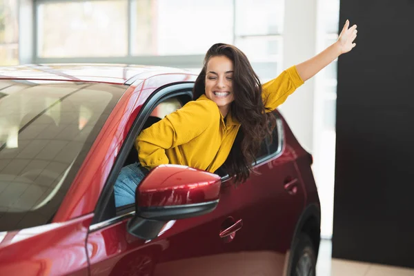 Bella donna bruna in cerca di nuova auto nel centro di concessionaria che sporge dal finestrino del veicolo — Foto Stock