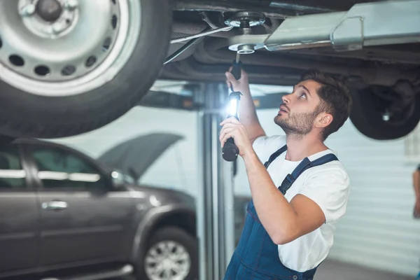 Giovane bel meccanico che lavora nel reparto assistenza auto fissaggio telaio del veicolo — Foto Stock