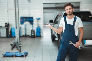genç yakışıklı mekanik elinde spanner ile üniforma giyen araba servis merkezinde modern ekipman gösteren