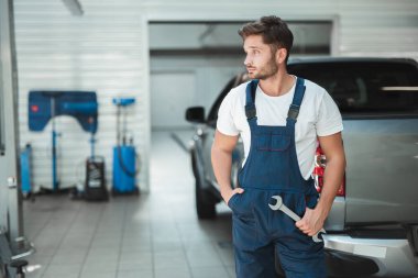 genç seksi mekanik cebinde bir el ve başka bir elinde anahtar ile üniforma giyen araba servis merkezinde duruyor