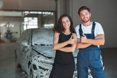 Üniforma giyen genç yakışıklı bir adam ve güzel bir kadın müşteri araba yıkama istasyonunda tabela gibi duruyorlar.