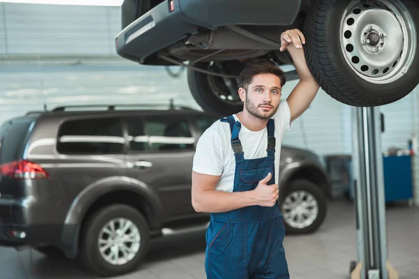 Joven mecánico guapo que trabaja en el departamento de servicio de coches se siente feliz mostrando como signo — Foto de Stock