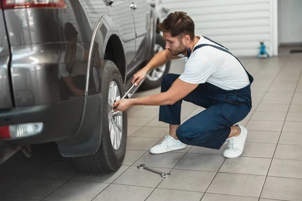 Joven mecánico guapo con uniforme de trabajo en el departamento de servicio de automóviles la fijación de neumáticos pinchados con llave — Foto de Stock