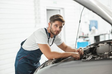 Araba kaputunda motor tamir eden üniformalı genç yakışıklı tamirci servis bölümünde çalışıyor.