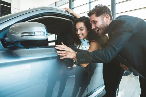 Hombre guapo y joven hermosa mujer buscando feliz comprobar el interior del coche nuevo al elegir un coche nuevo en el centro de concesionarios — Foto de Stock