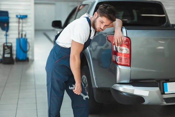 Joven mecánico cansado con uniforme apoyado en el maletero de recogida en el centro de servicio de automóviles — Foto de Stock