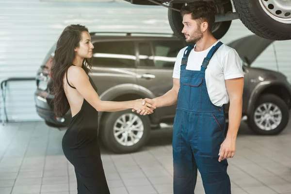 Joven mecánico guapo y hermosa mujer cliente estrechando la mano en gratitud por el gran servicio proporcionado — Foto de Stock