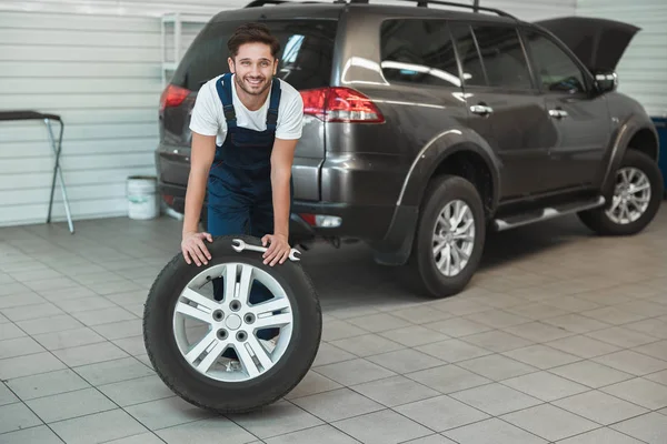 Joven mecánico guapo que trabaja en el departamento de servicio de coches la fijación de neumáticos pinchados se ve satisfecho — Foto de Stock