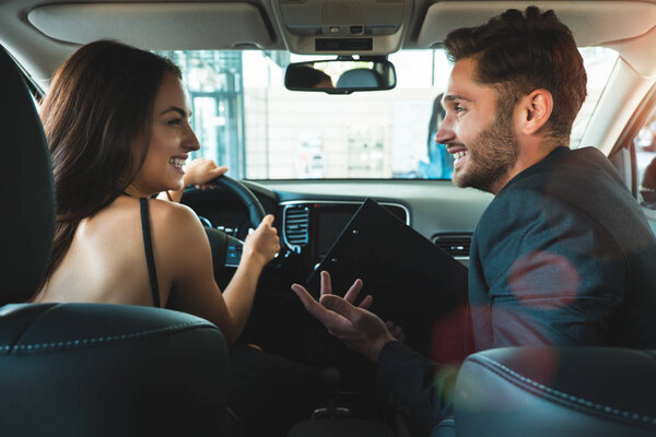 handsome man and young beautiful woman checking new car interior while choosing new car in dealership center