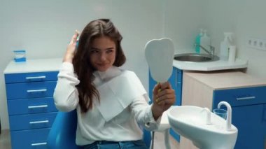 Genç, güzel, esmer kadın hasta dişçide otururken aynada dişlerine dokunmasını izlemekten memnun görünüyor.