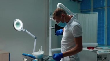 Komik, genç, yakışıklı dişçi çalışma yerinin yanında mutlu bir şekilde dans ediyor. Ofisinde tıbbi eldiven ve maske takıyor.