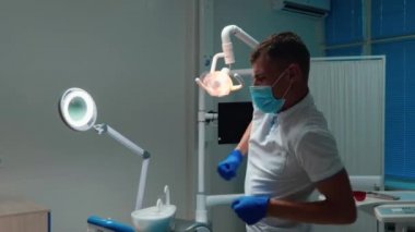Komik, genç, yakışıklı dişçi çalışma yerinin yanında duygusal olarak dans ediyor. Ofisinde maske ve eldiven takıyor.