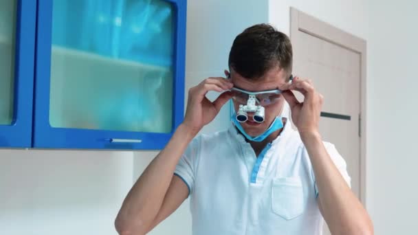 Mladý lékař nošení drhnutí upravuje jeho zubní brýle na klinice — Stock video