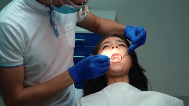 Dentiste dans les gants guérit les patients femmes dents en utilisant miroir dentaire et barrage lors de rendez-vous dans une clinique dentaire — Video