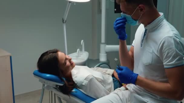 Happy doctor dentist takes off his medical mask and glove and gives five to pleased with result patient woman both smiling — Stock Video