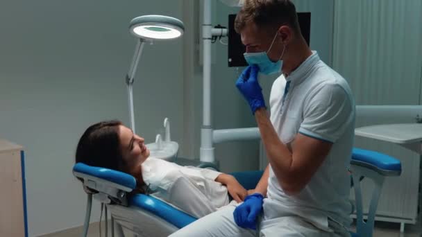 Young happy doctor dentist takes off his medical mask and glove and gives five to pleased with result patient woman both smiling — Stock Video