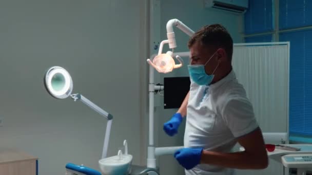 Divertente giovane medico dentista bello ballare emotivamente vicino al suo posto di lavoro indossando guanti medici e maschera nel suo studio — Video Stock