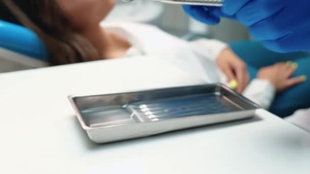 Οδοντίατρος με ιατρικά μπλε γάντια παίρνει όργανα και αρχίζει να θεραπεύει τα δόντια των γυναικών ασθενών χρησιμοποιώντας οδοντικό καθρέφτη και φράγμα κατά τη διάρκεια του ραντεβού στην οδοντιατρική κλινική — Αρχείο Βίντεο