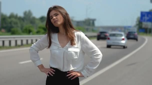 Schöne junge brünette Frau versucht, vorbeifahrende Autos auf der Straße zu stoppen — Stockvideo