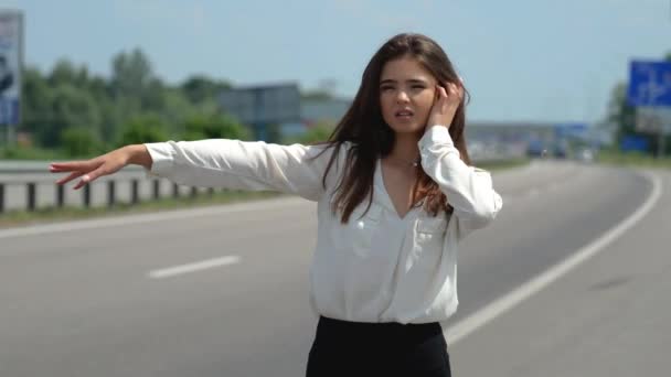 Красивая молодая брюнетка женщина пытается остановить проезжающие мимо машины на дороге выглядит отчаянно — стоковое видео