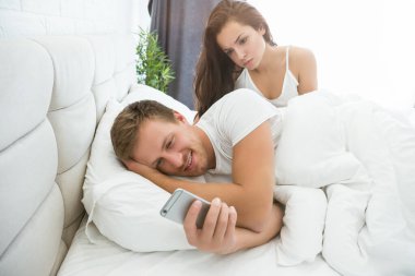 Cep telefonlu yakışıklı bir adam yatakta genç ve güzel bir kadınla yatıyor.