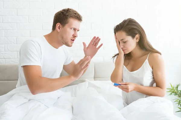 Young couple quarrelling handsome man crying at young beautiful woman who is holding pregnancy test — Stock Photo, Image