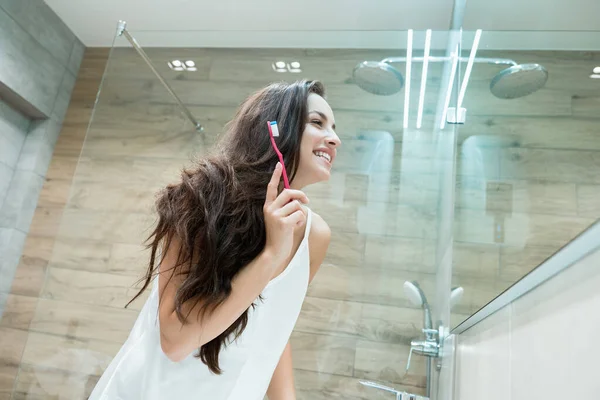 Giovane bella donna in piedi davanti allo specchio del bagno mentre si lava i denti — Foto Stock
