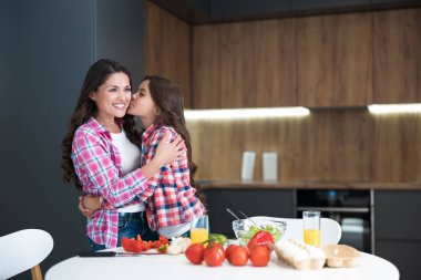 Genç, güzel bir kadın ve tatlı kızı mutfakta kahvaltı hazırlıyorlar. Mutlu bir şekilde öpüşüyorlar.